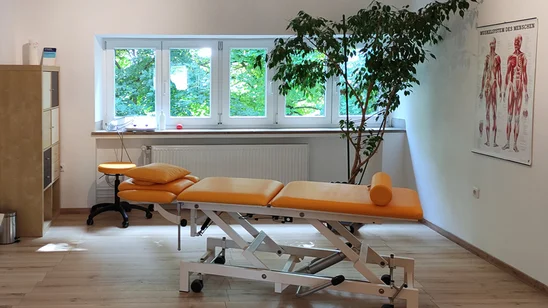 Behandlungsraum mit oranger Therapieliege, Rollhocker und Anatomieposter